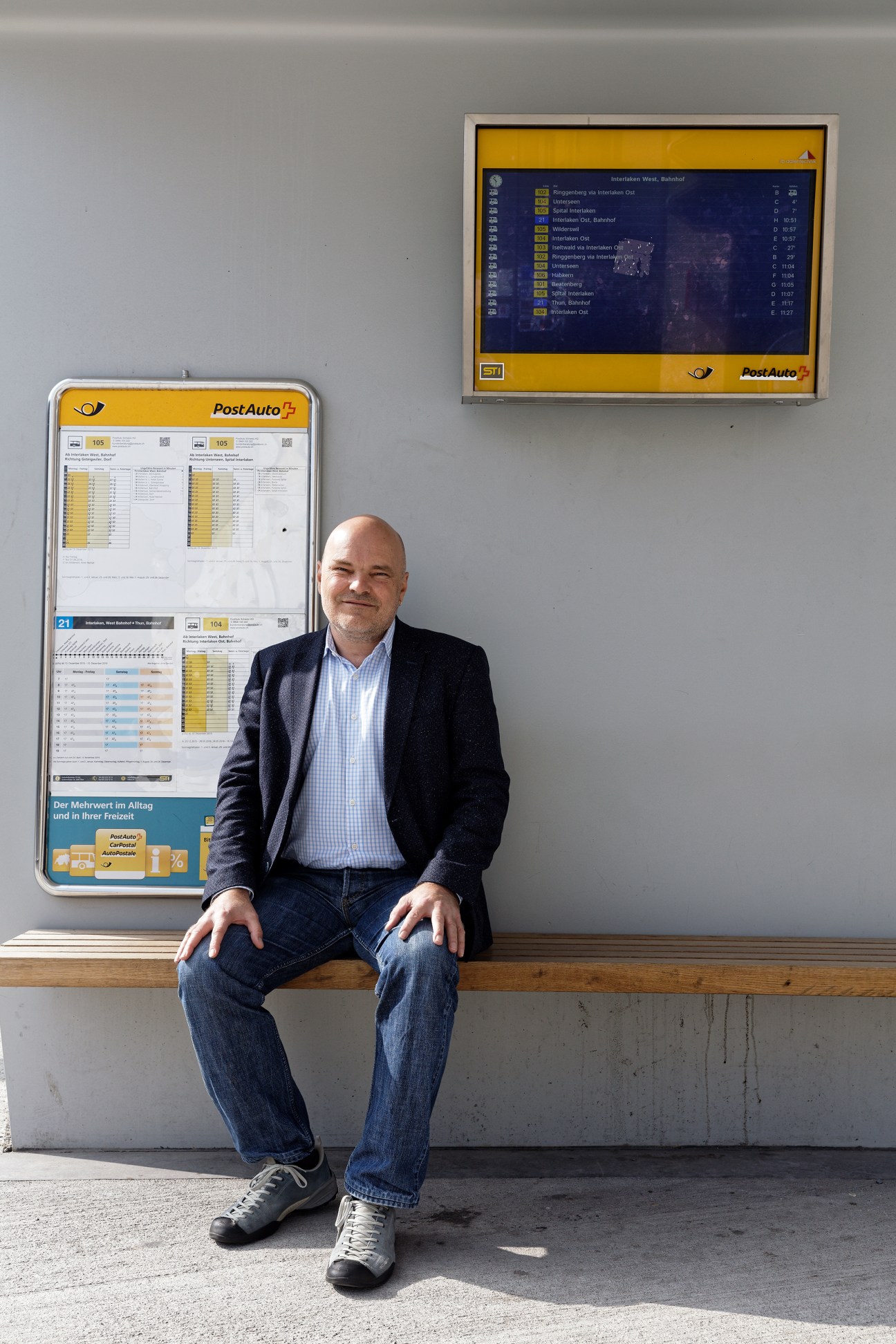 Ruedi Simmler, director of the Bern region for PostAuto, sits in front of PostAuto timetable displays.