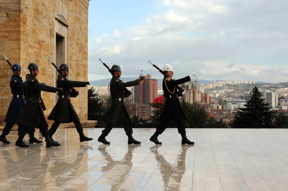 Soldiers marching outside the Anitkabir mausoleum in Ankara with rifles and city skyline visible.