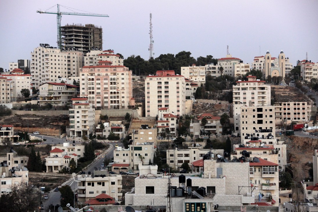 Construction cranes tower over densely packed apartment buildings with red-tiled roofs in Ramallah.