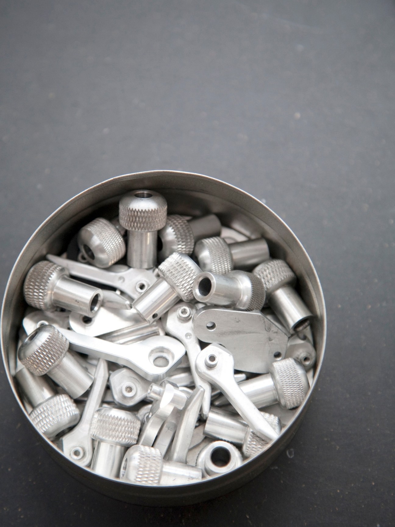 Metal prototype parts and screws for Alpa cameras arranged in a circular container.