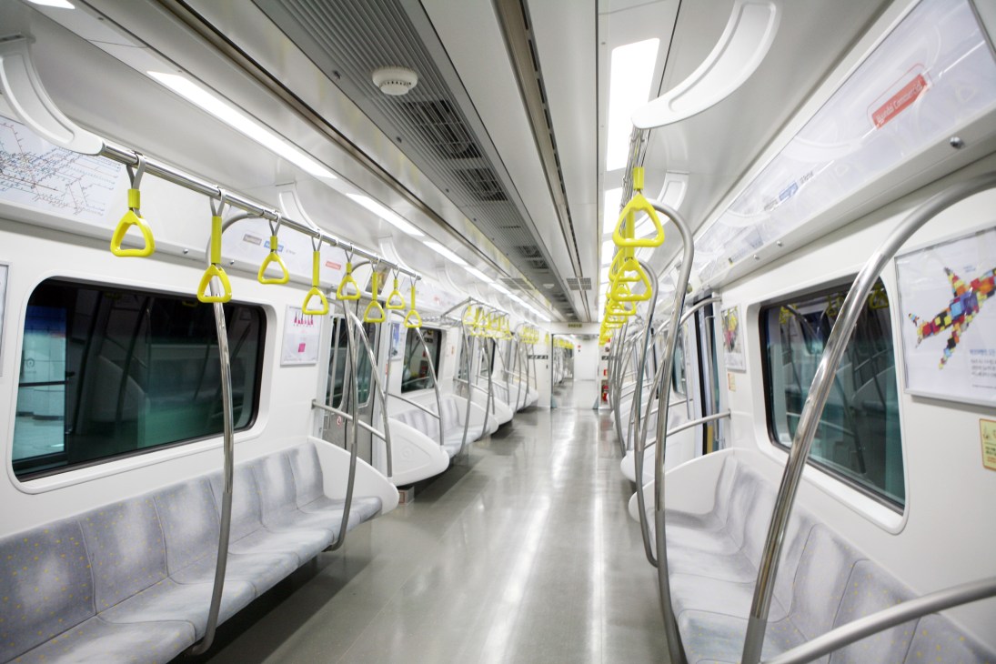 Interior of a Seoul subway car with yellow handholds and minimal white advertisements on walls.