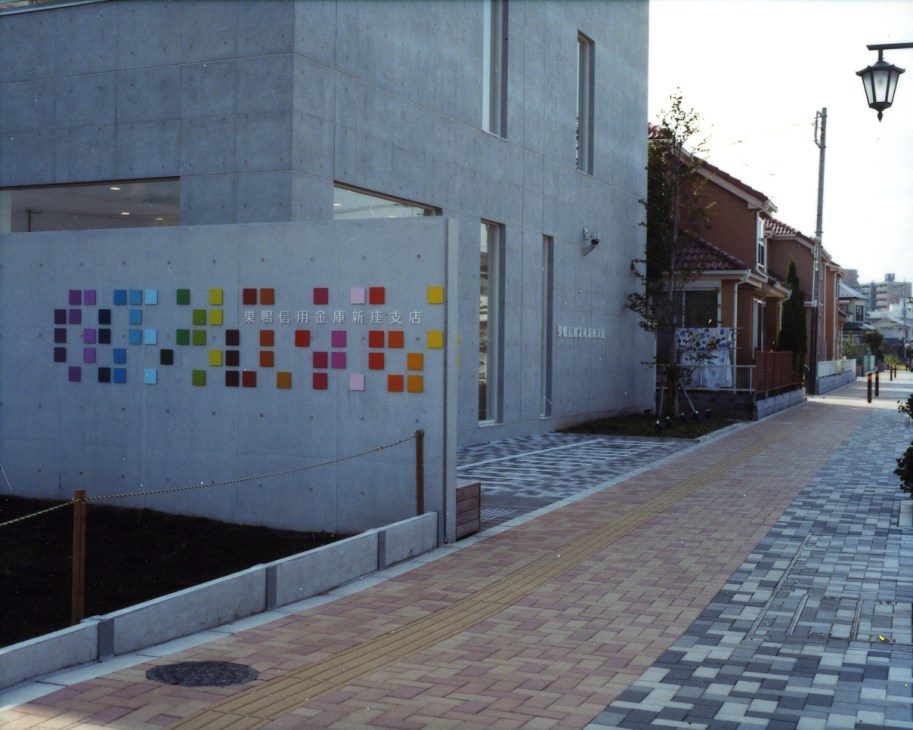 Gray concrete bank building with colorful square logo mosaic on facade, viewed from street.