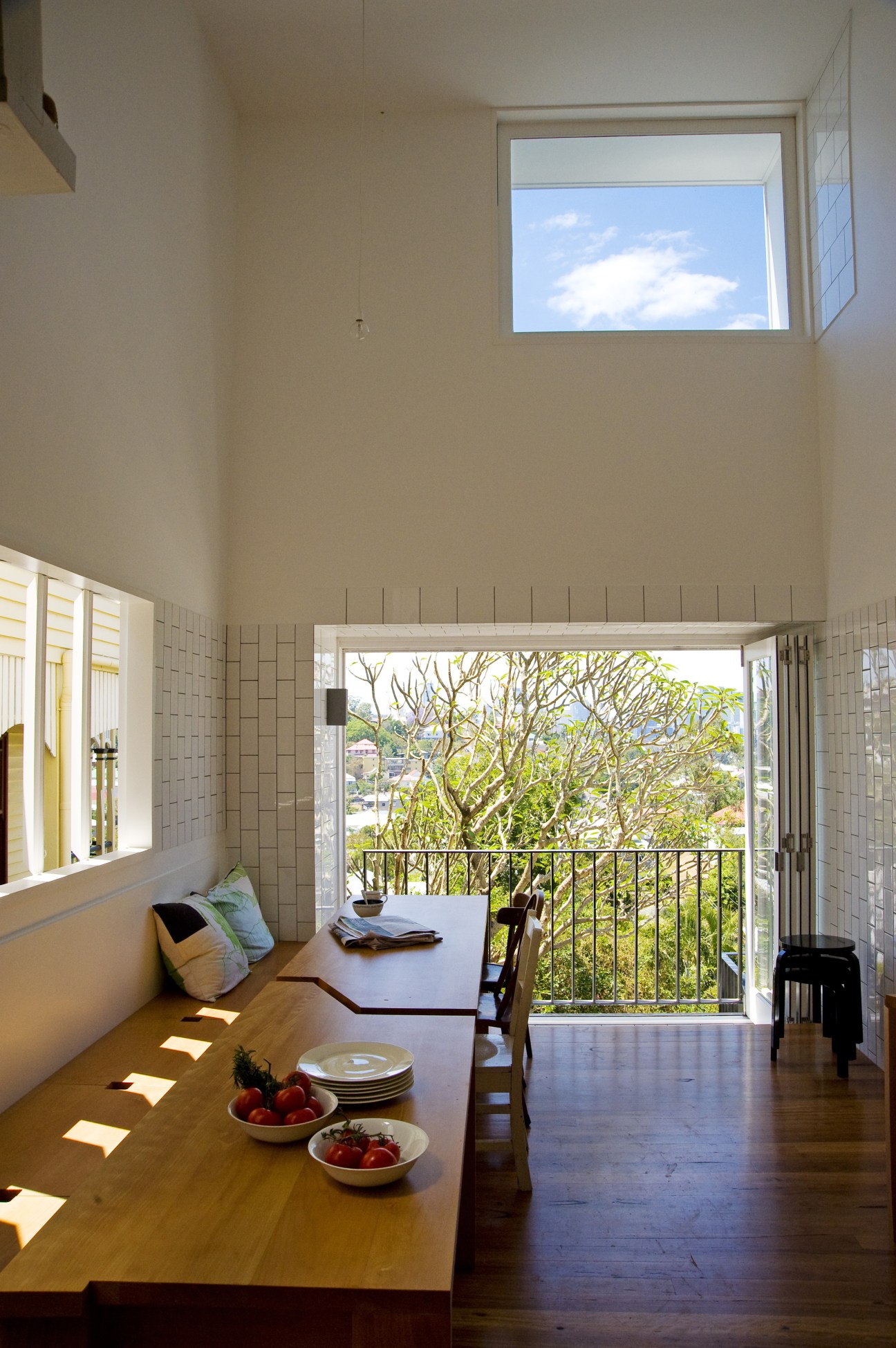 Dining room with wooden table, butchers' tiles, window seat, and views of Brisbane through glass doors to a balcony.