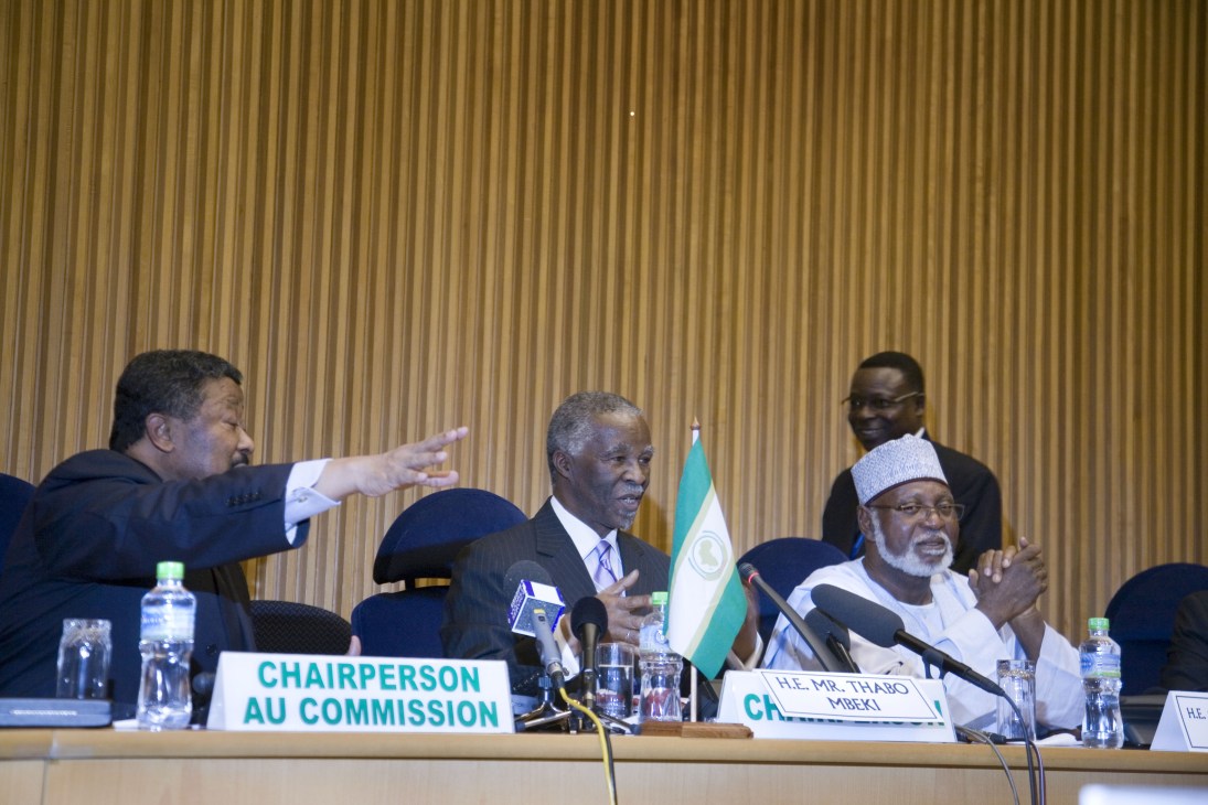 AU Chairperson Jean Ping gestures while speaking at a conference table next to South Africa's Thabo Mbeki.