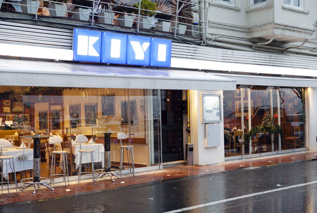 Kiyi restaurant storefront with blue neon sign, large windows, and modern interior seating visible from street.