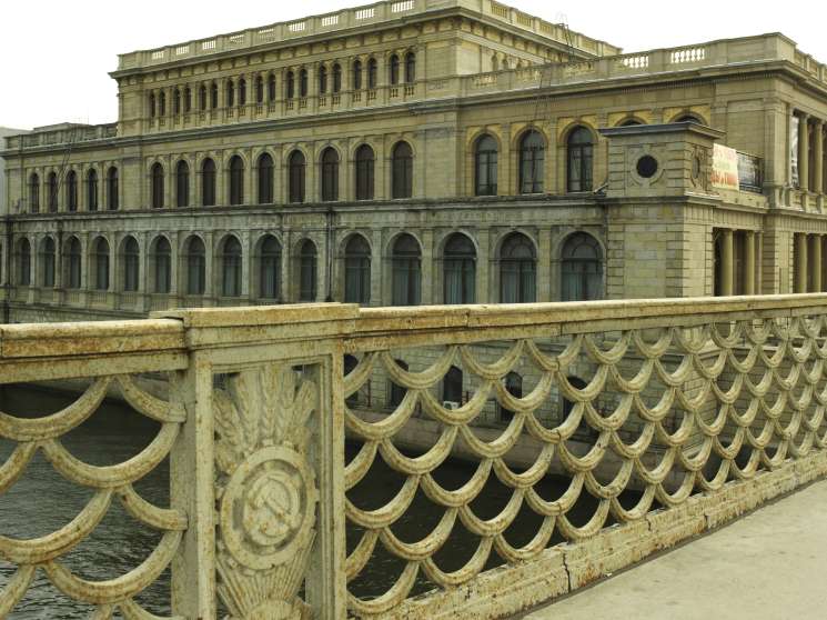 Soviet-era bridge with ornate railings over the Pregol river, former German stock exchange building behind