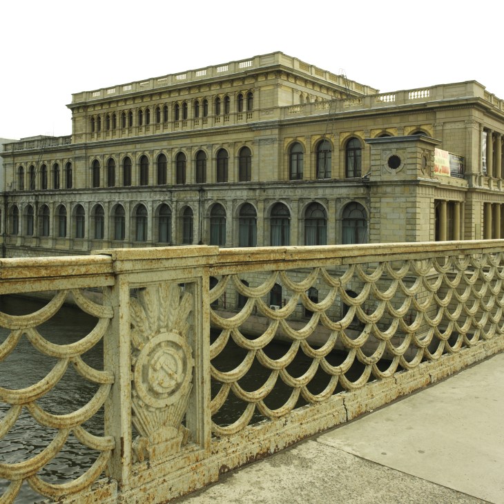 Soviet-era bridge with ornate railings over the Pregol river, former German stock exchange building behind