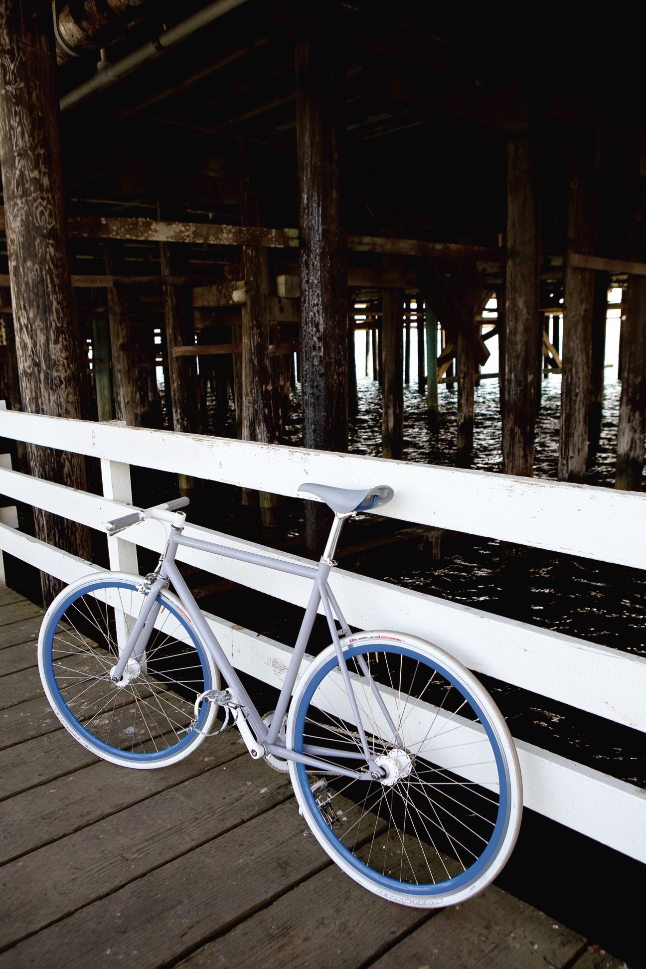 Globe's Roll bike with white frame and blue wheels resting on a white railing on a wooden pier.