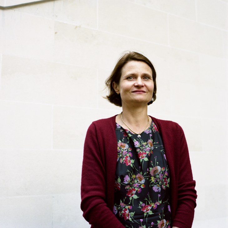 Woman wearing a burgundy cardigan over a black floral dress against a white wall.