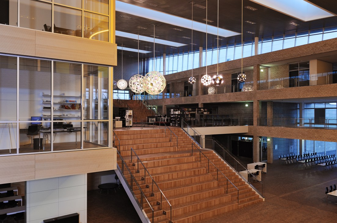 Central wooden staircase in AP Møller School with tiered seating, glass balconies, and pendant lights above.
