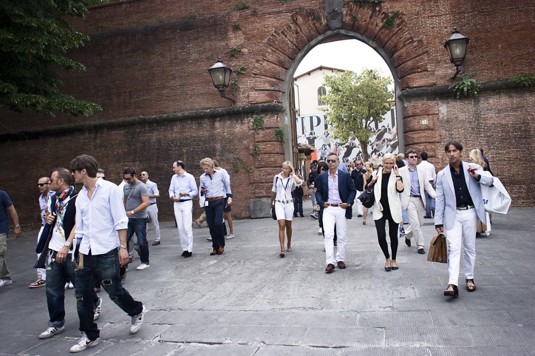 Attendees walking through an arched brick gateway at Pitti Uomo menswear fair in Florence.