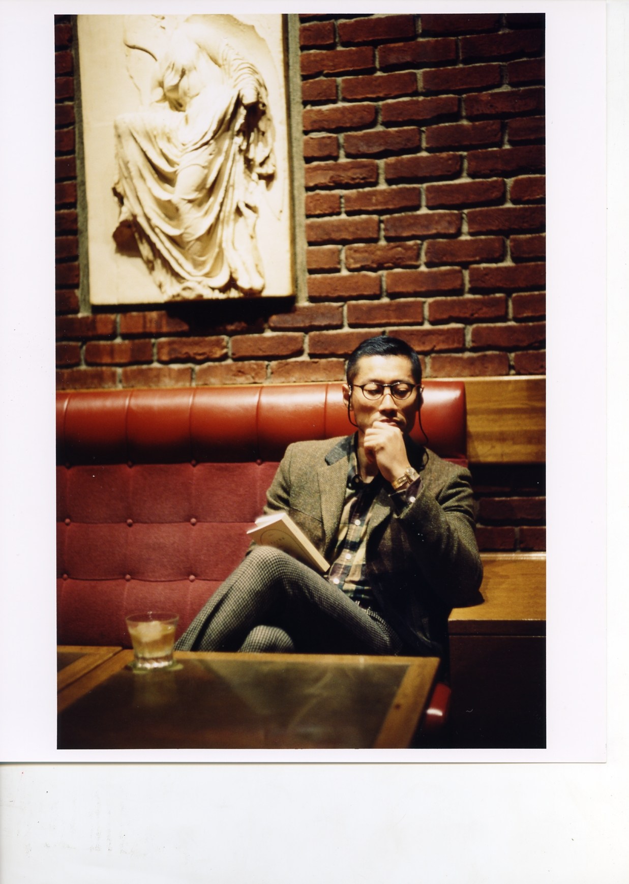 Man in glasses and olive jacket seated on red leather banquette at Brillant Bar, Tokyo.