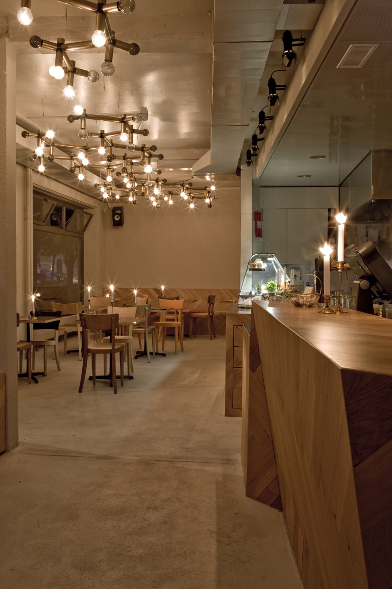 Interior of Z am Park Café in Zürich showing wooden counter, tables with chairs, and brass branching light fixtures.