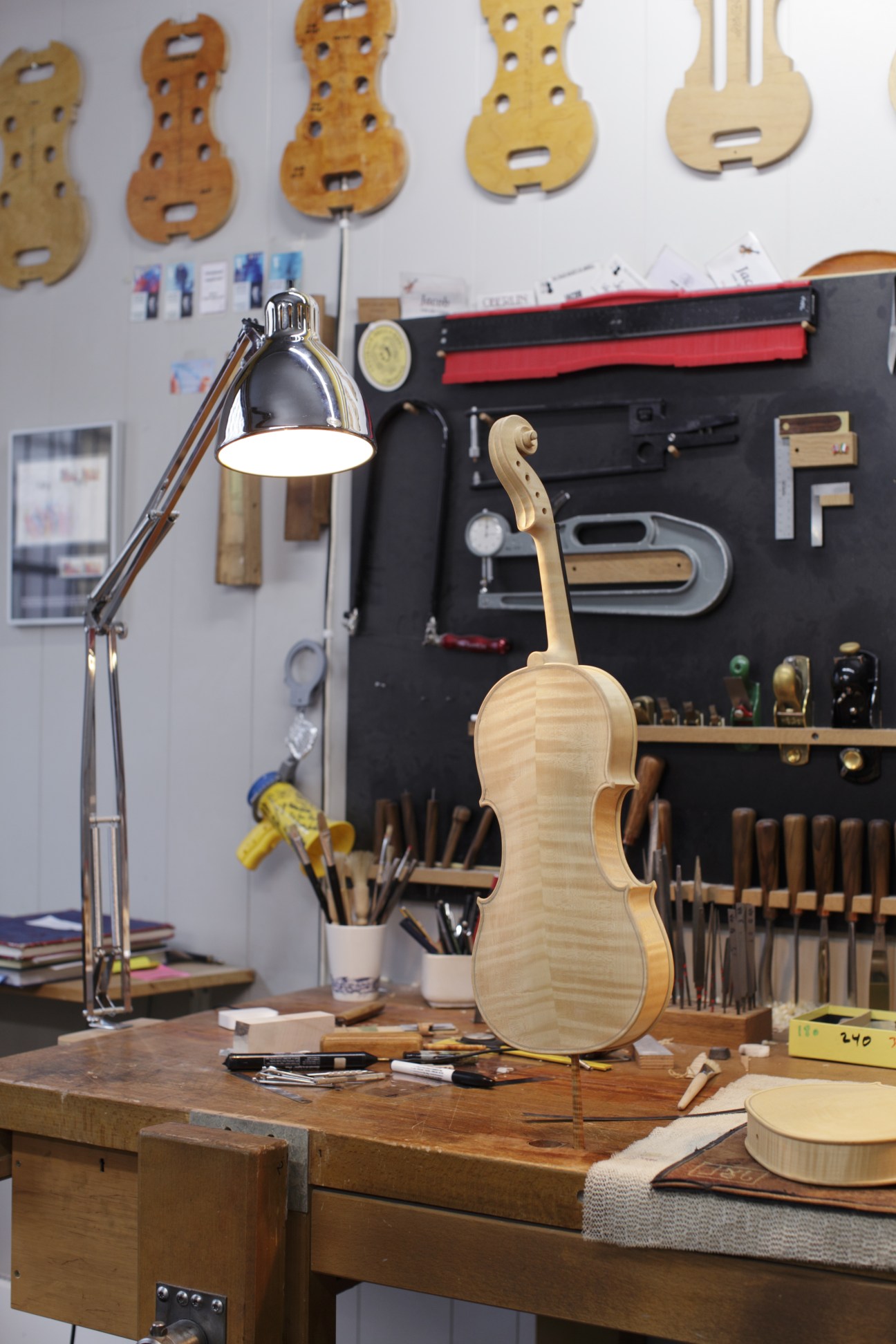 Jacob von der Lippe's violin workshop showing a wooden violin on a workbench with tools and violin parts on the walls.