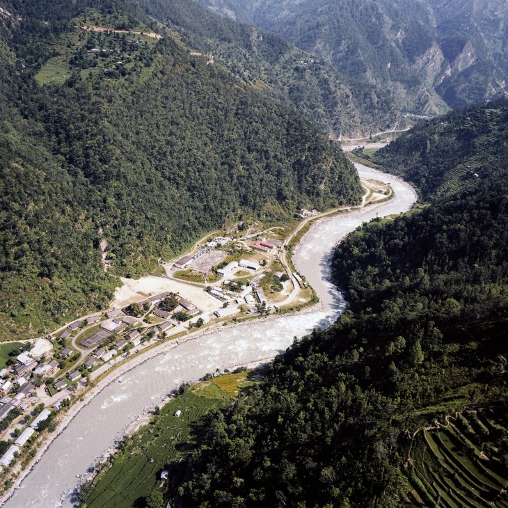 Aerial view of the Khimti hydropower plant nestled in a forested river valley in Nepal's mountains.