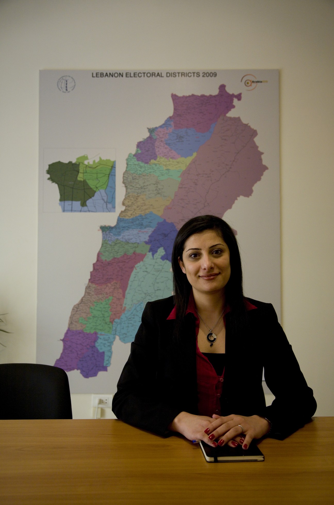 Chantal Sarkis, IFES programme manager, seated at desk with Lebanon electoral districts map behind her.