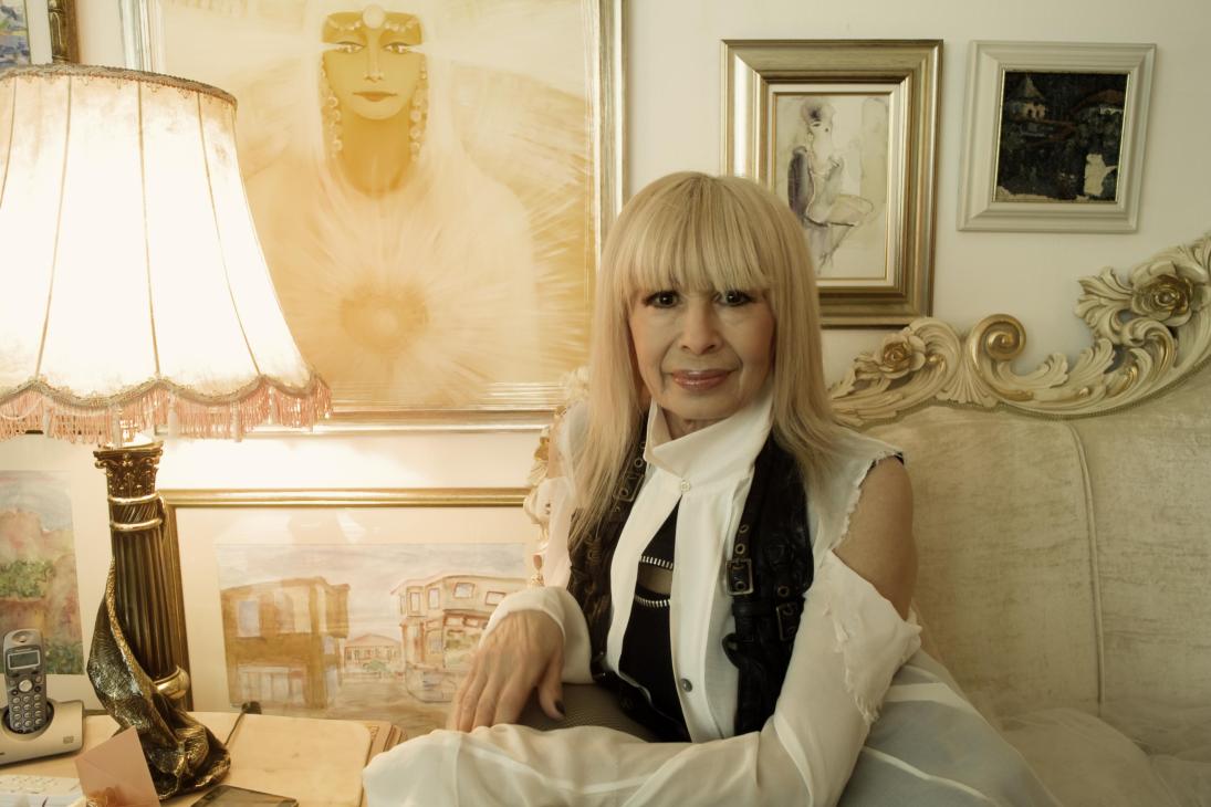 Bulgarian singer Lili Ivanova sits at a desk in her ornately decorated Sofia apartment surrounded by framed artwork and decorative sculptures.