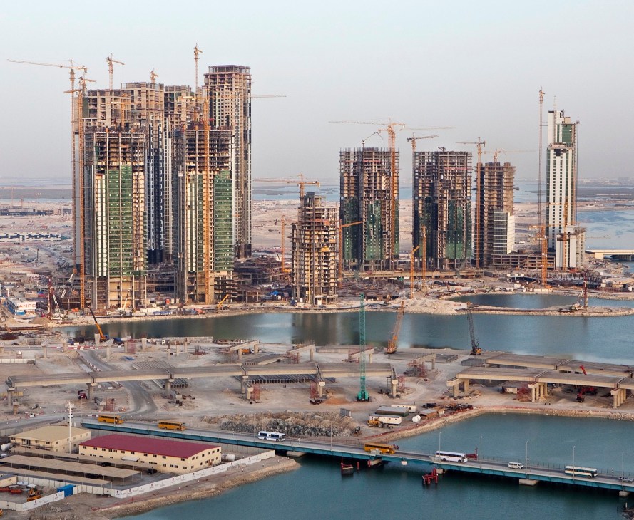 Aerial view of Abu Dhabi's skyline with multiple high-rise buildings under construction surrounded by numerous yellow cranes.