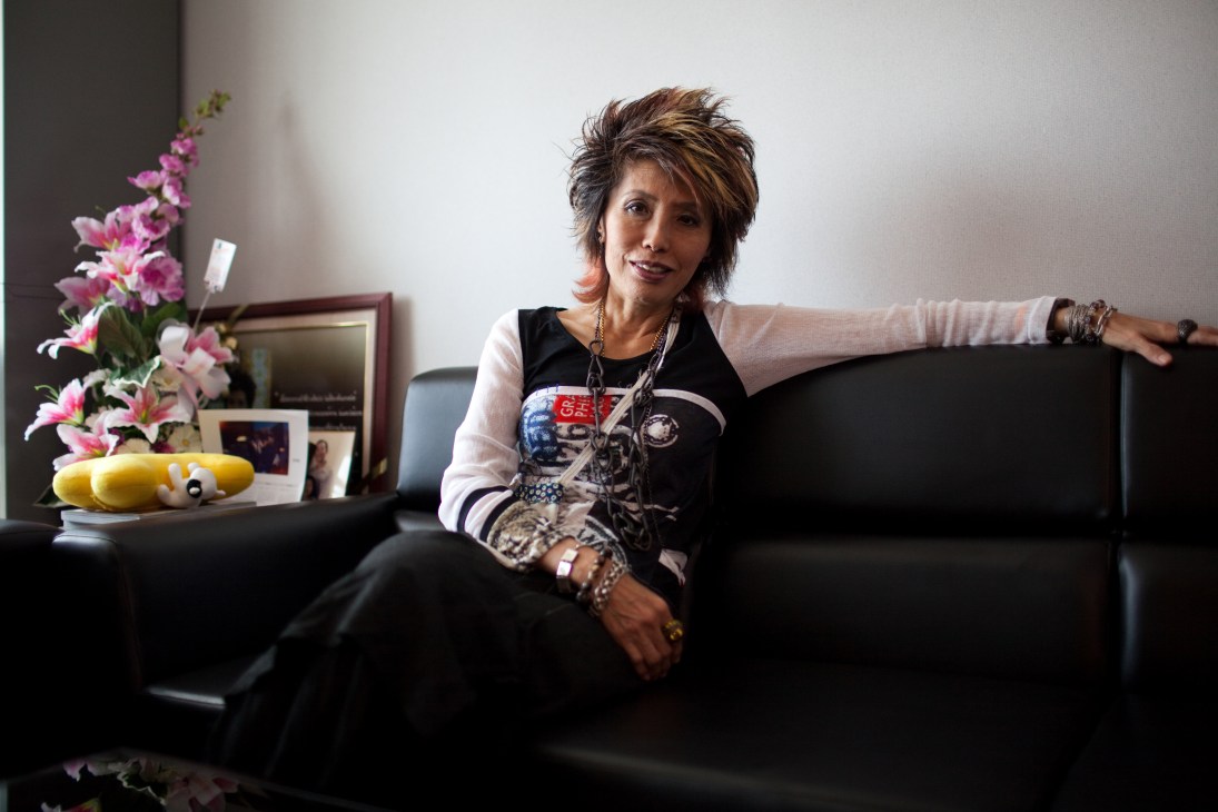 Forensic scientist Porntip Rojanasunan sitting on a black lounge chair in her Bangkok office, wearing a black and white top with chains and bracelets.