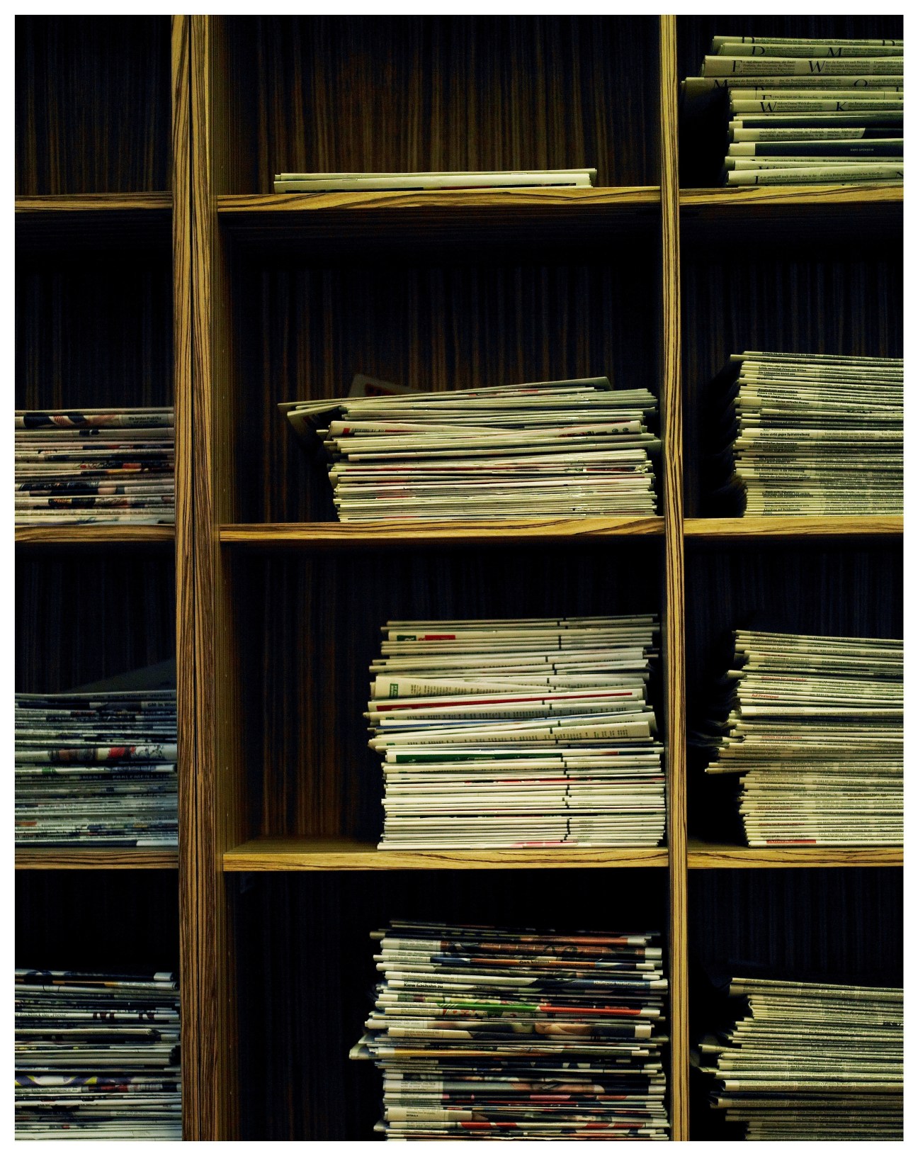 Stacked magazines displayed on wooden shelves with brass dividers against a dark striped background.