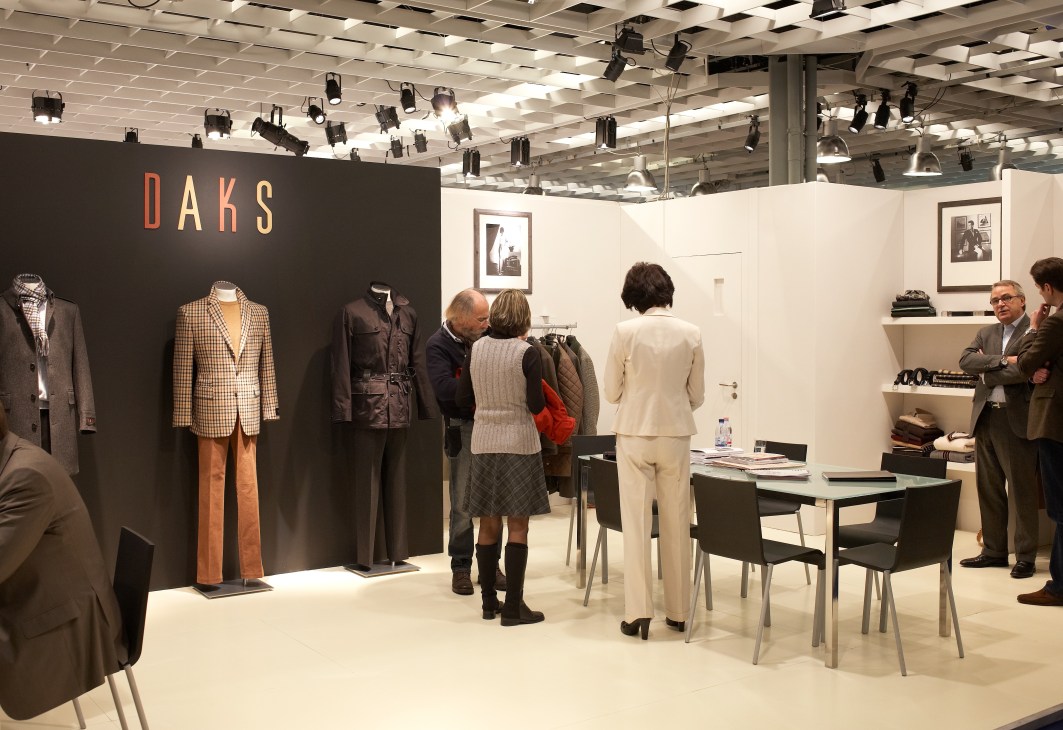 Daks menswear showroom display with checked blazers, orange trousers, and black jackets on mannequins at Pitti Immagine Uomo.