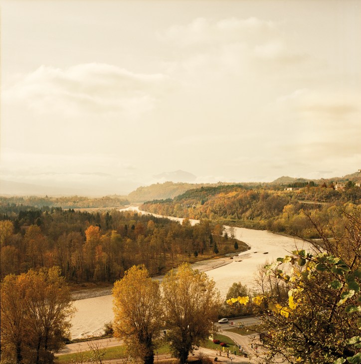 Autumn landscape view of the Piave river winding through forested valley with Dolomite mountains in distance.