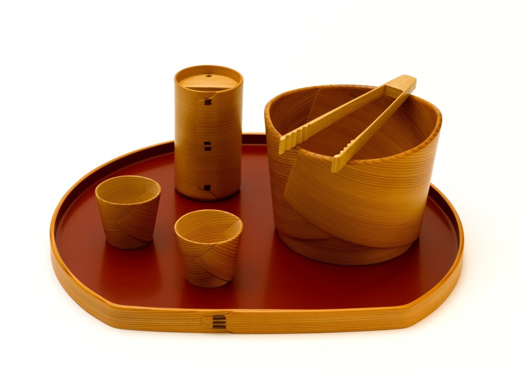 Kurikyu bentwood homeware set featuring a red tray, wooden vessels, cups and cylindrical container with handles.