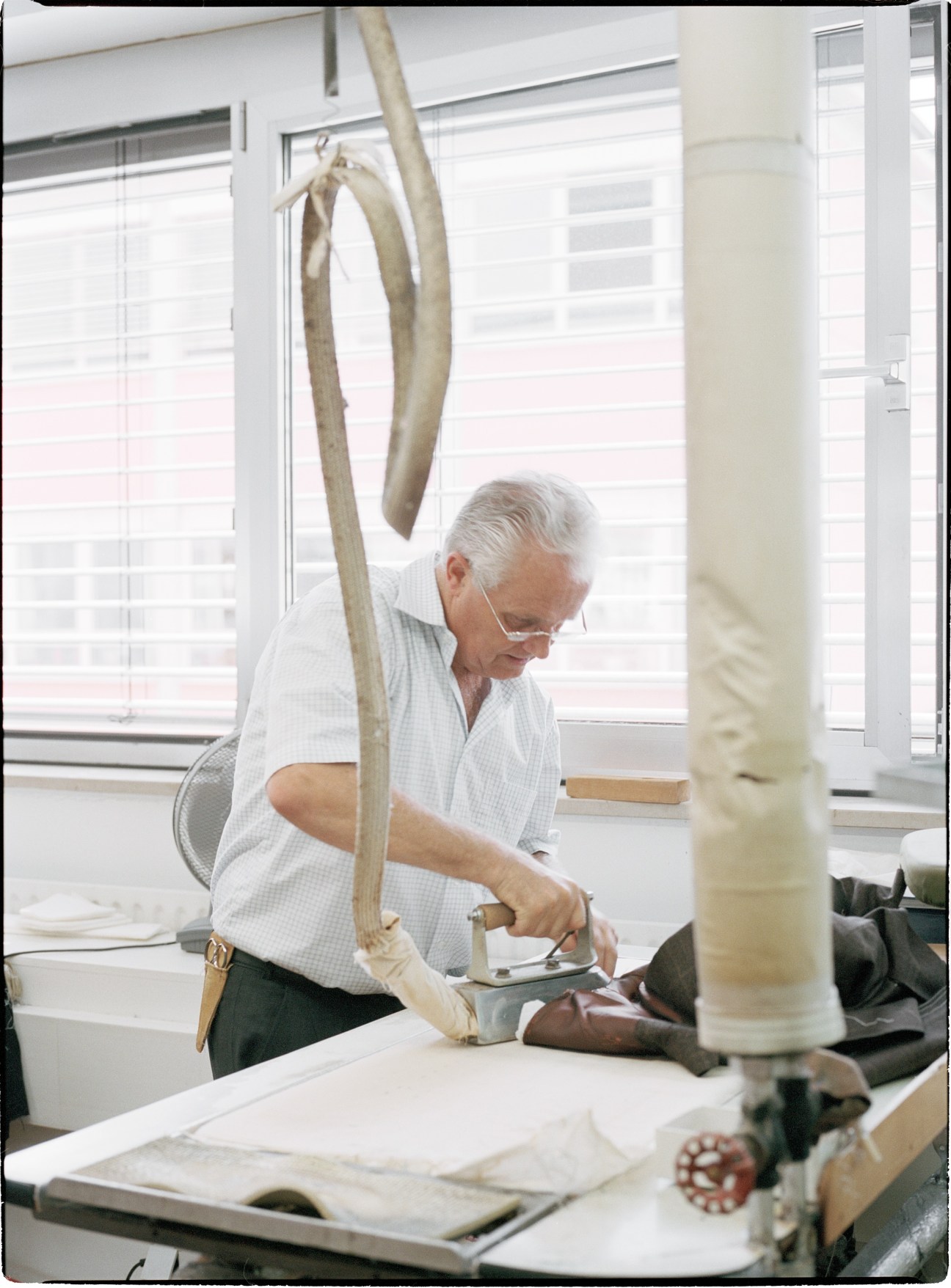 Older man in light blue shirt pressing fabric on a work table at Regent tailoring studio.