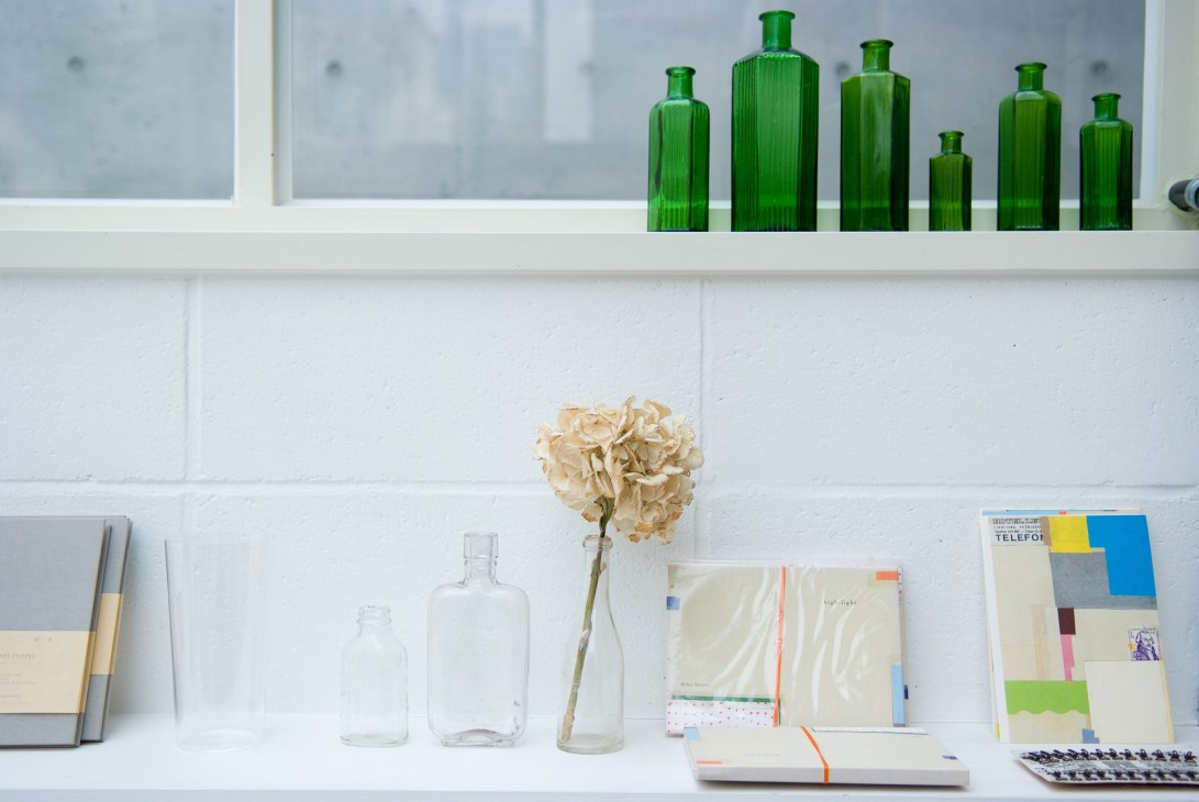 White shelving with green glass bottles on top shelf and dried flower with clear bottles on lower shelf.