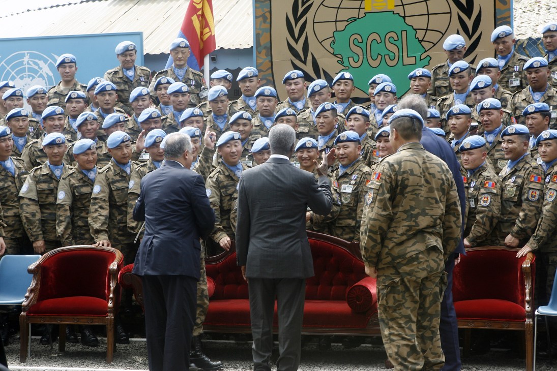 Kofi Annan in dark suit addresses Mongolian UN peacekeeping troops wearing blue berets in Sierra Leone.