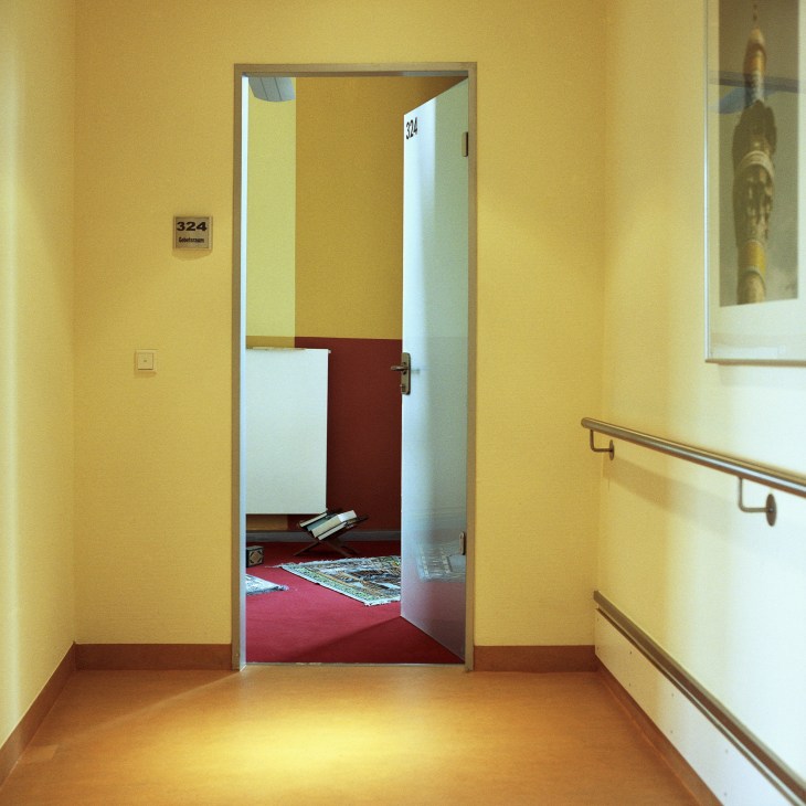 Prayer room with prayer mat and Islamic texts in a hospital corridor at Hamburg's UKE medical centre.