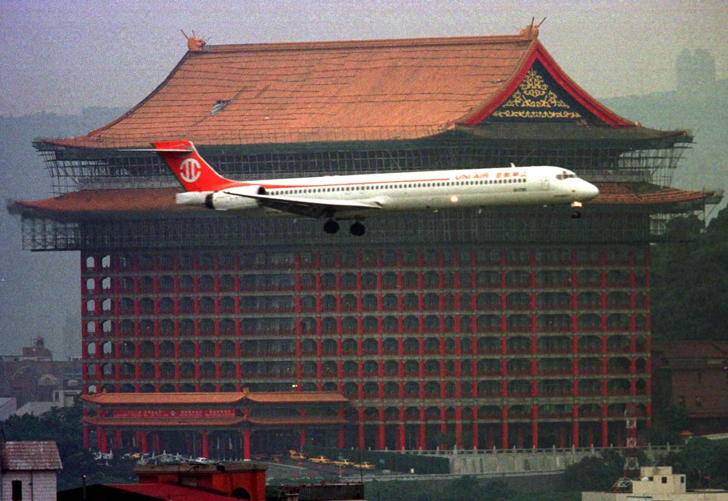 Taiwan airline aircraft with red tail flying past traditional Asian architecture building.