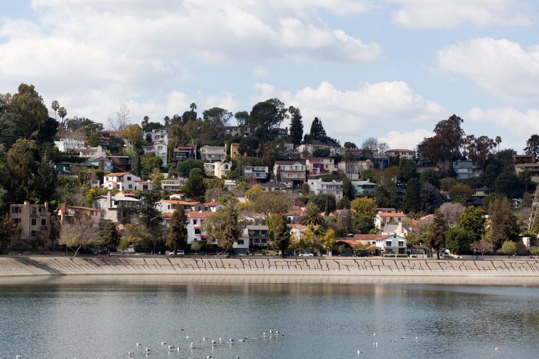 Colorful residential houses built on hillside overlooking Silver Lake Reservoir with trees and blue sky.