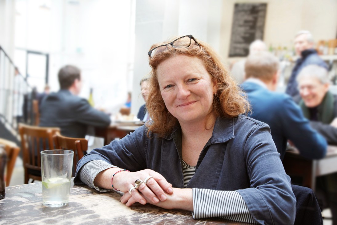 Rachel Whiteread sits at a table in St John restaurant, smiling at the camera with a glass of water in front of her.