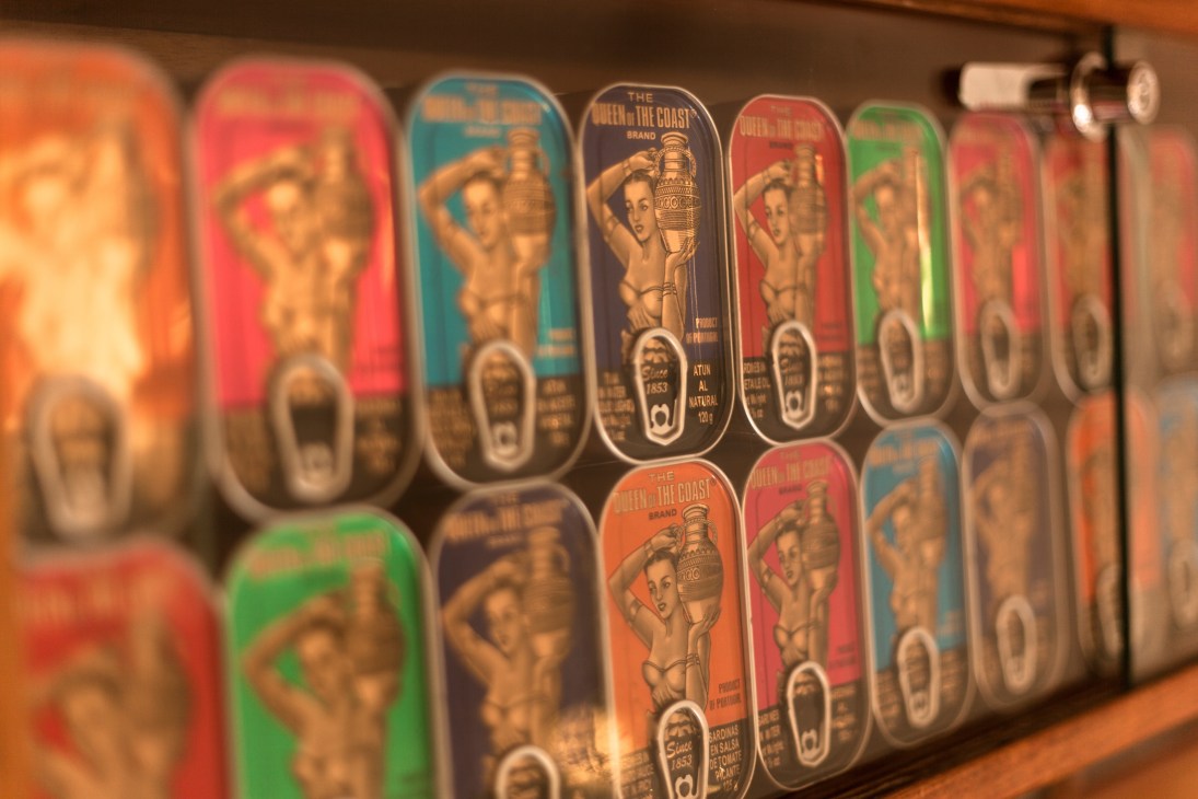 Colorful vintage canned fish tins displayed on wooden shelf with art deco-style labels.