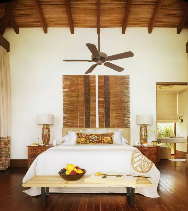 Luxury bedroom with wooden beams, ceiling fan, white bedding, and tropical decor at Mukul resort.
