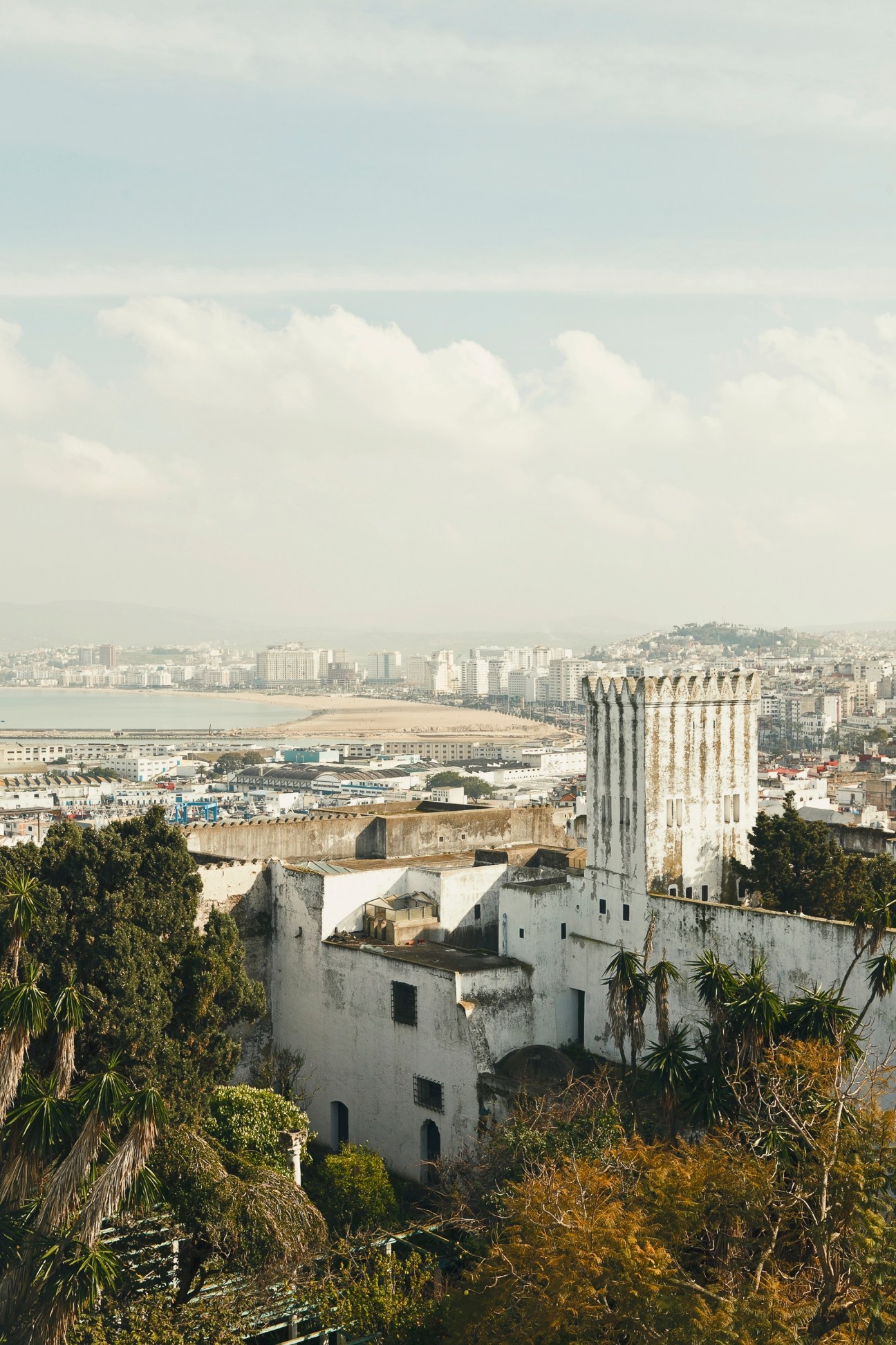Tangier's cityscape viewed from the Kasbah rooftop, showing historic white buildings, beach, and Mediterranean coast.