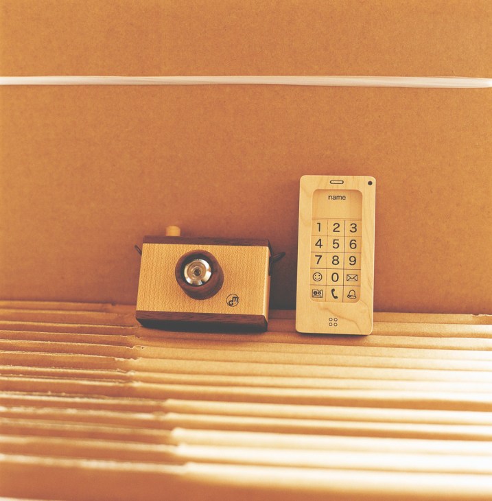 Wooden toy camera and phone on wooden strips against an orange background.