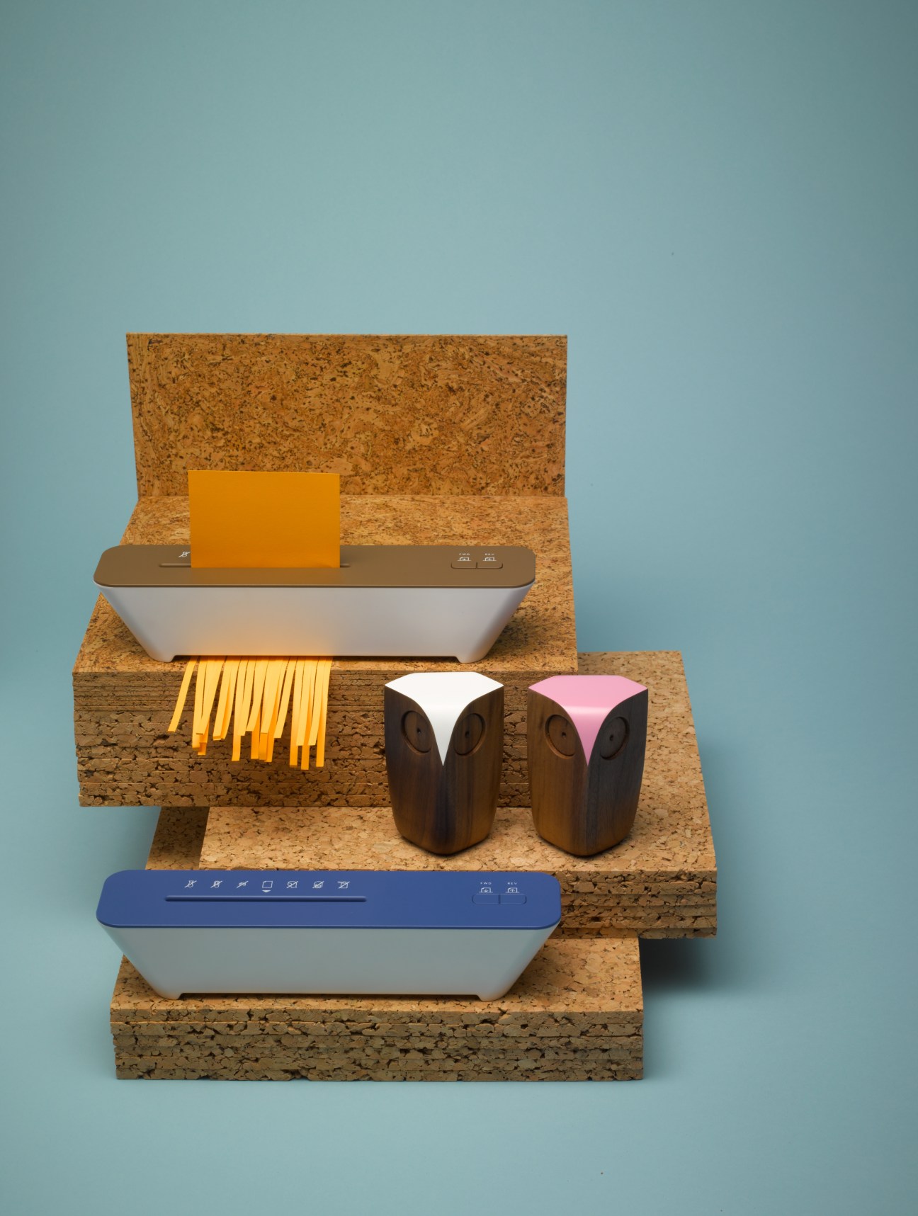 Styled display of an IDEA paper shredder and Matt Pugh wooden owls arranged on cork platforms against a blue background.
