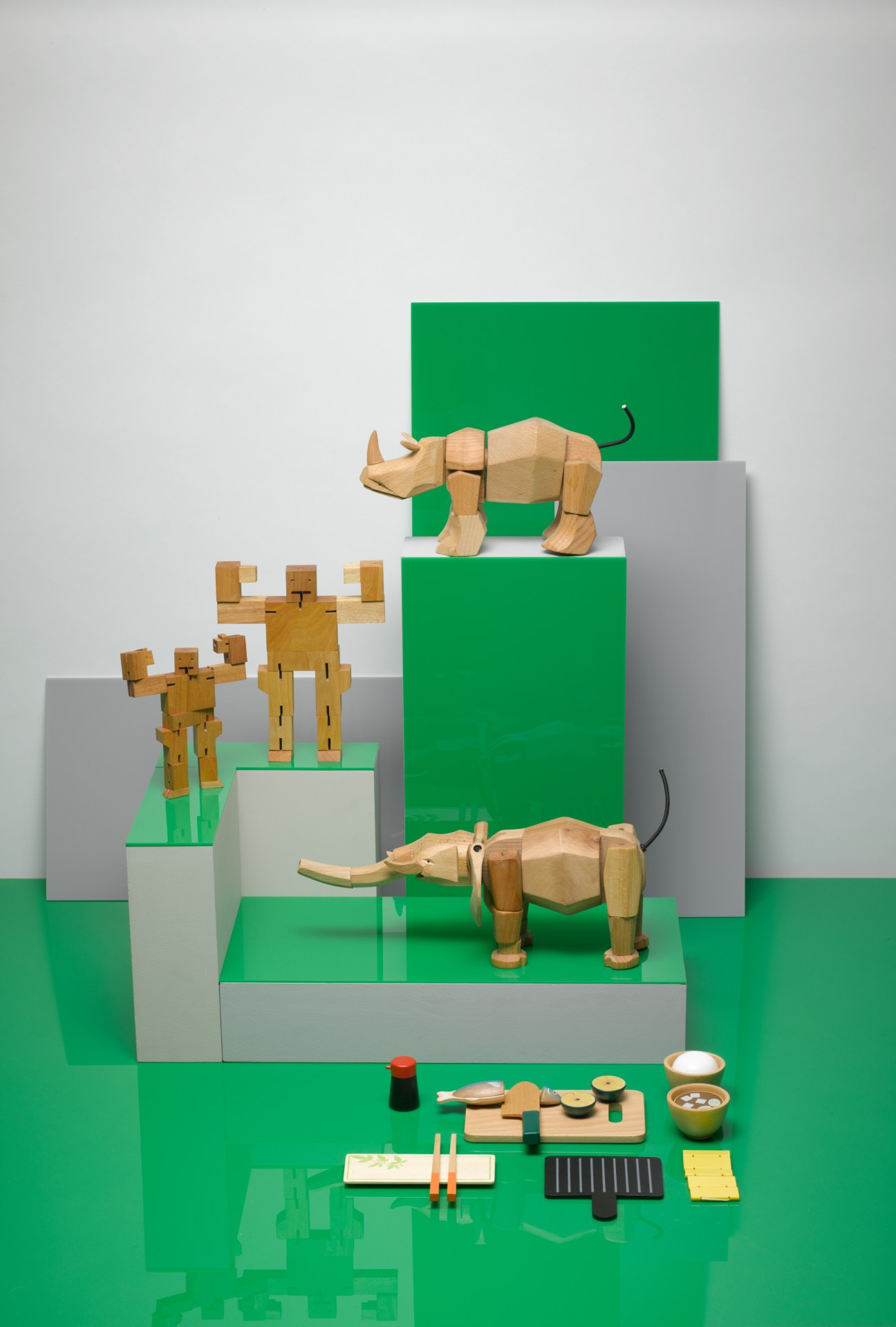 Wooden articulated animal toys by David Weeks including rhino, elephant, gorilla and bear with magnetic joints, displayed with Woody Puddy cooking toys on green platform.