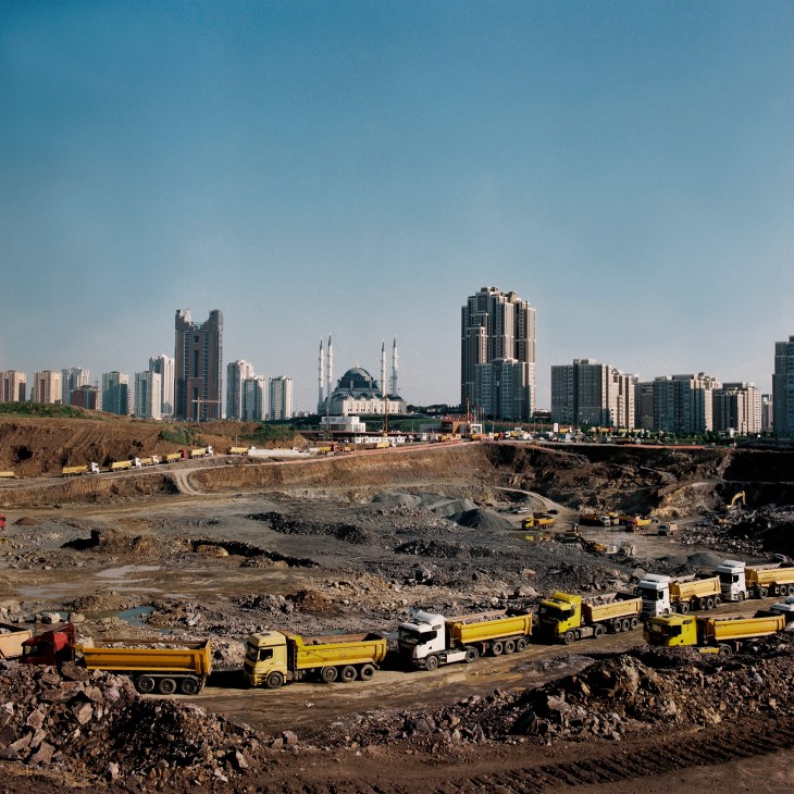 Excavation site for Istanbul's new financial centre with yellow dump trucks and earthmoving equipment against the city skyline.