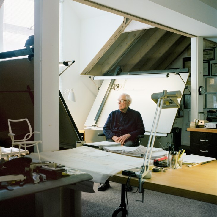 Niels Diffrient sits at an architect's drawing board in his Connecticut studio, surrounded by design work and tools.