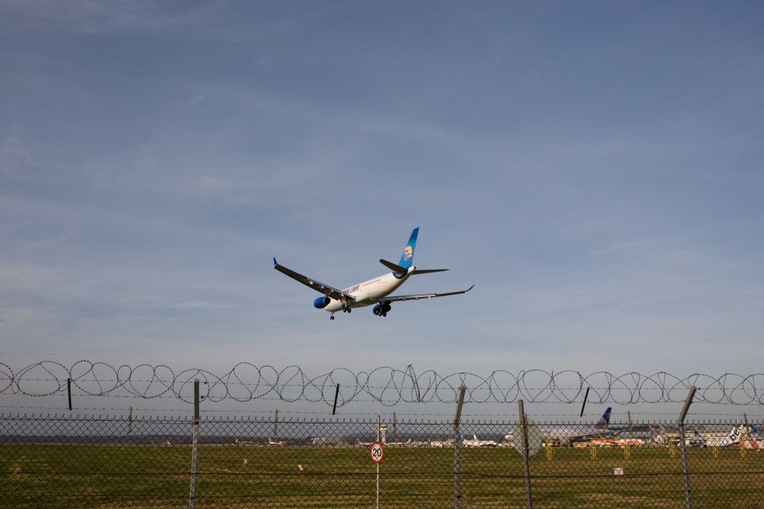 Commercial aircraft on approach to Gatwick Airport over perimeter fencing.