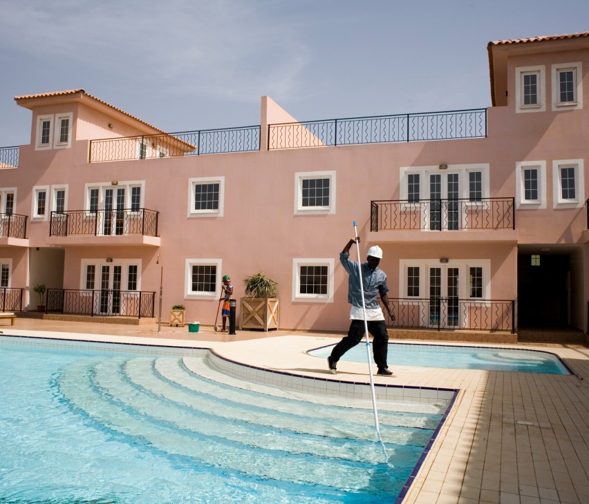 Pastel pink residential buildings with a swimming pool and workers at Sambala Village resort in Cape Verde.