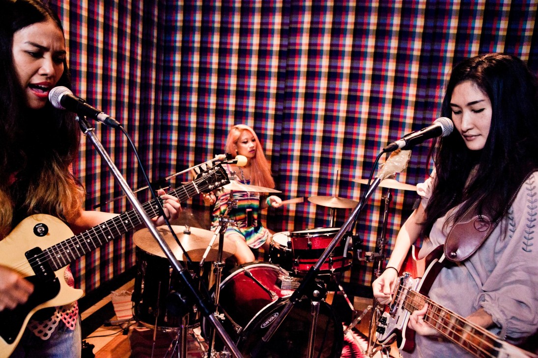 Yellow Fang band performs with three female musicians singing and playing guitars on stage with a colorful checkered backdrop.