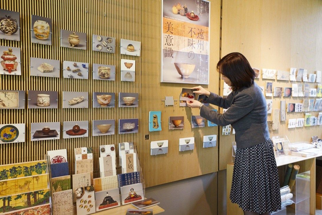 Woman arranging postcards on a display wall at the Nezu Art Museum gift shop.