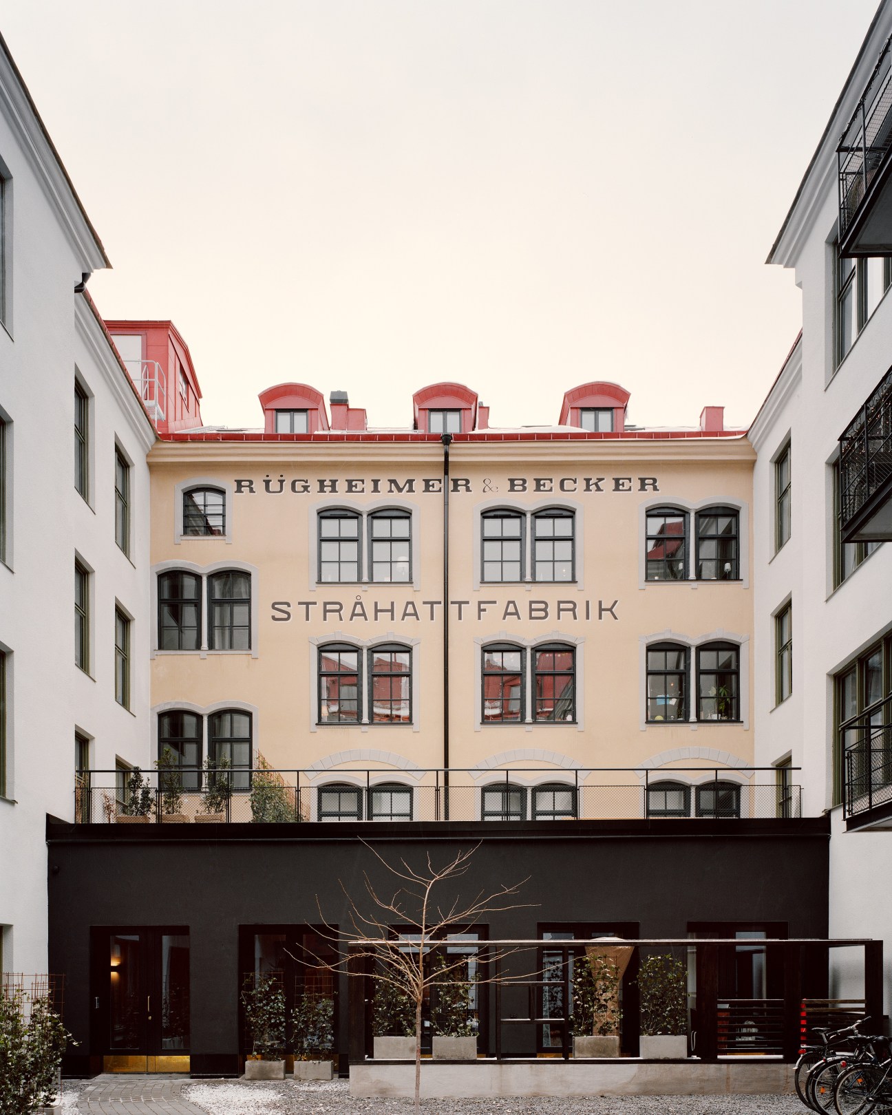 Courtyard view of renovated Stråhattfabrik building with restored peach-colored facade and red roof details