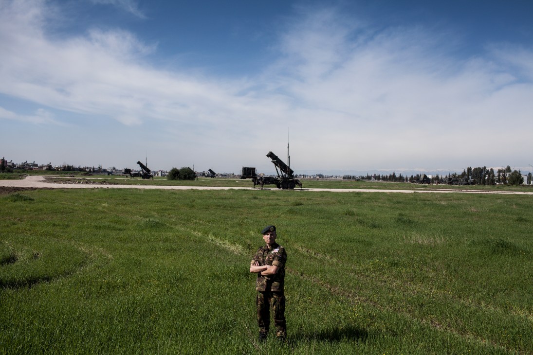 Dutch military officer standing in a green field with a Patriot missile launcher system in the background.
