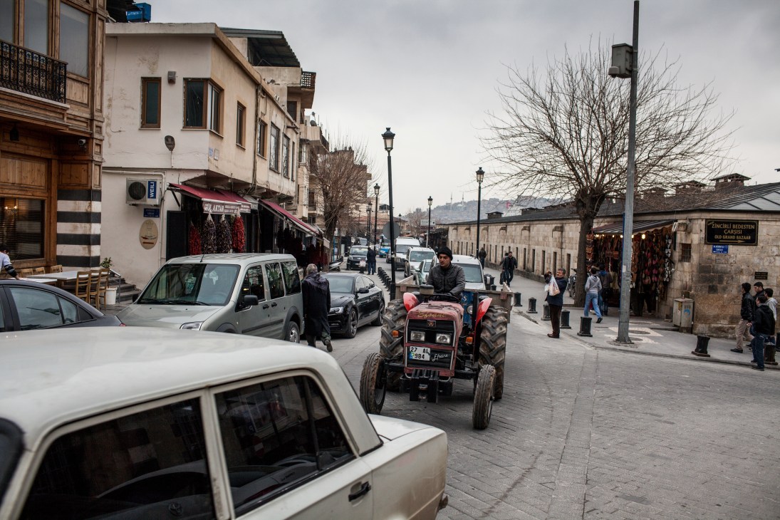 A red tractor drives through a historic cobblestone street in Gaziantep's old town marketplace.