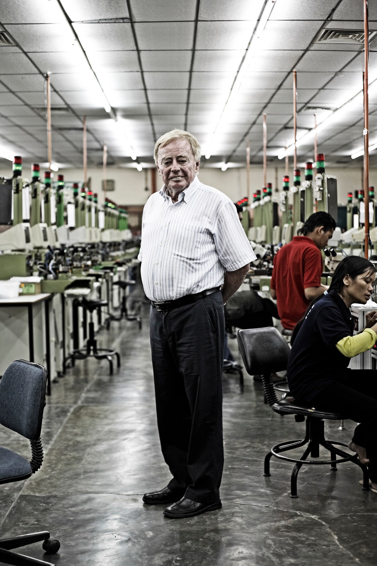 Gabor Faskerty stands in Fastron electronics factory production line with workers at machines.